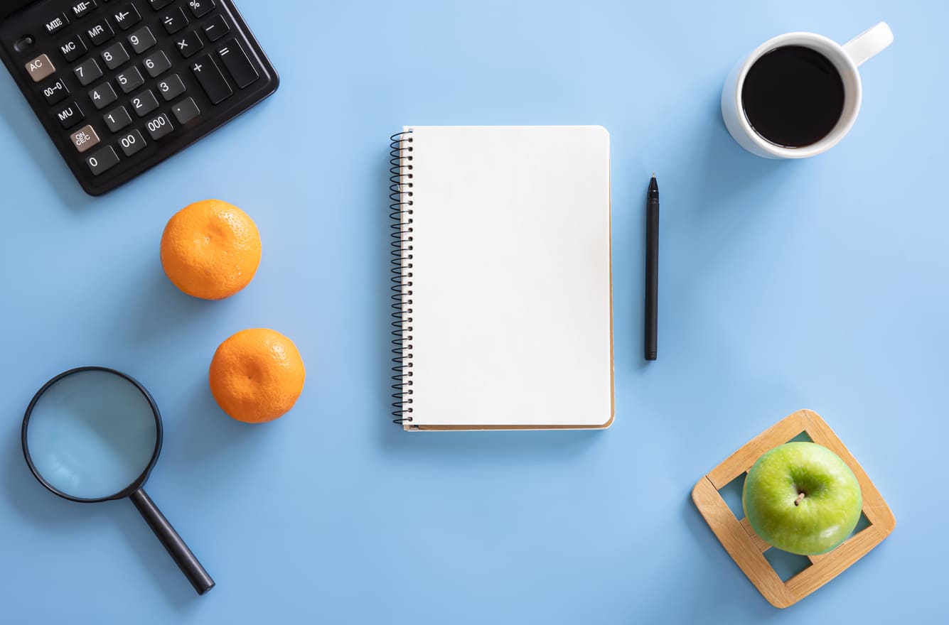 Cuaderno y alimentos saludables sobre un escritorio azul.